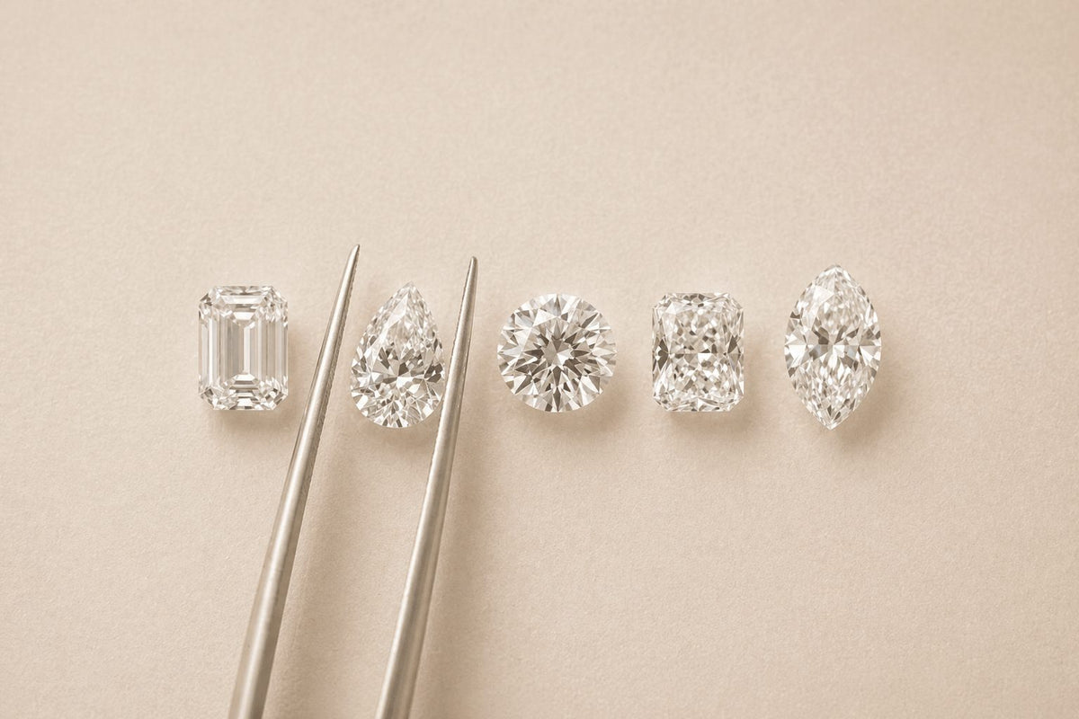 Cinq diamants de synthèse taille émeraude, poire, rond, coussin et marquise alignés près d'une pince