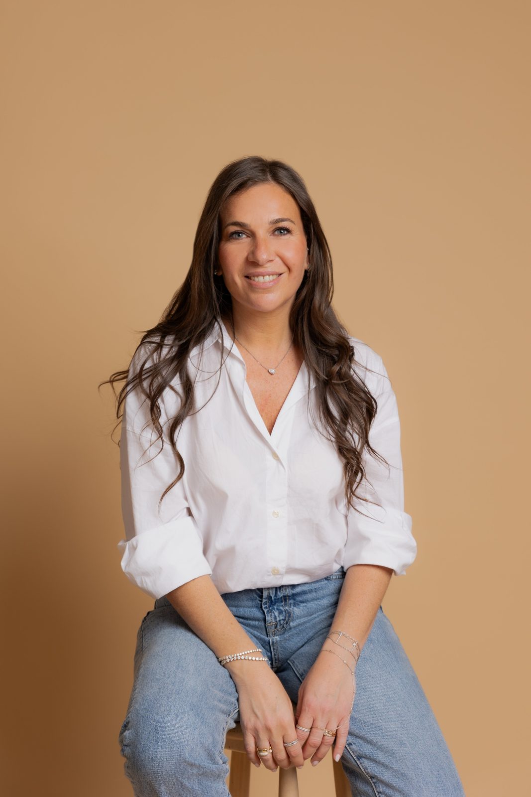 Jennifer, cofondatrice de NOELY-Diamant, souriante en chemise blanche sur fond beige