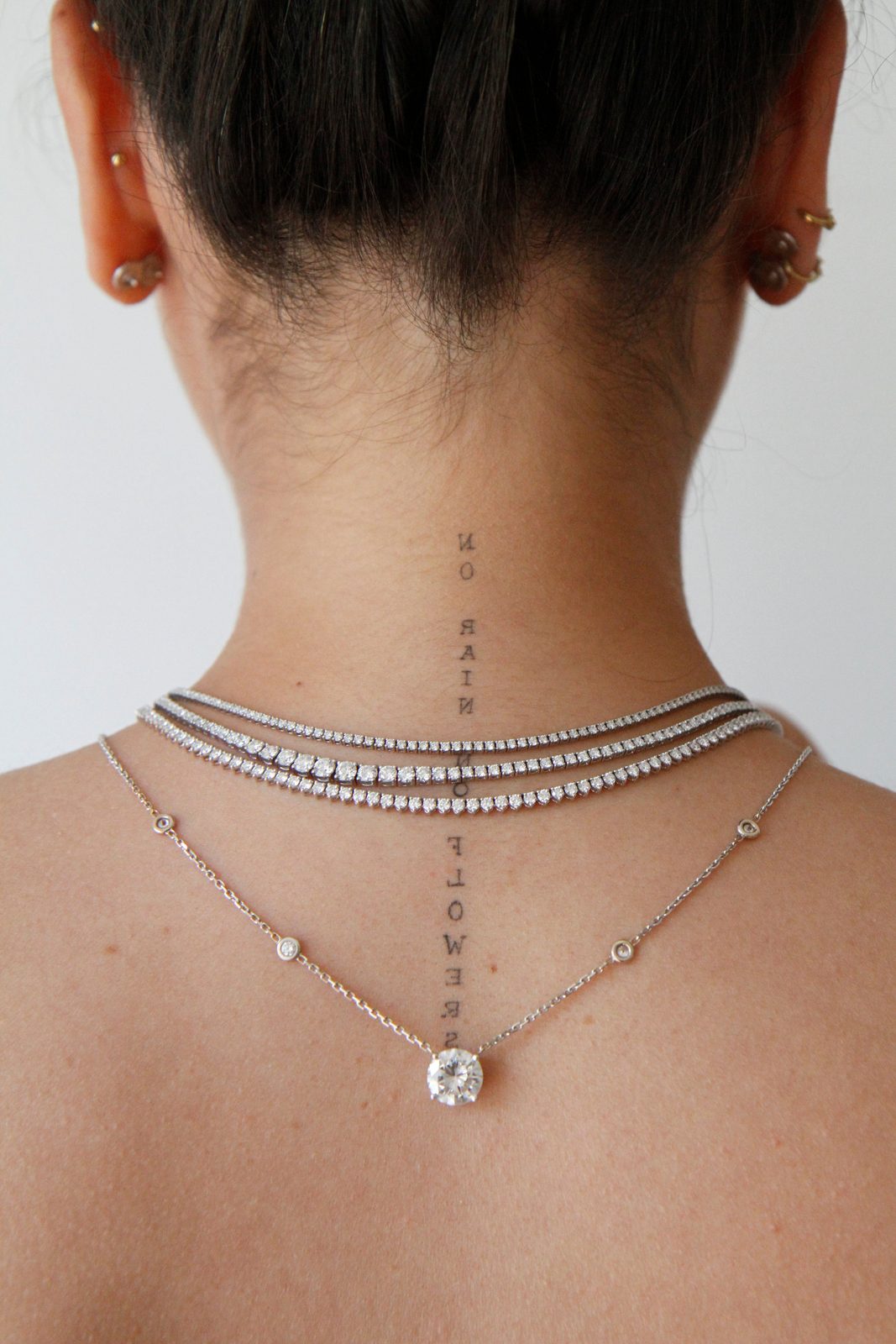 Nuque d’une femme portant trois colliers rivière de diamants et un pendentif solitaire sur chaîne