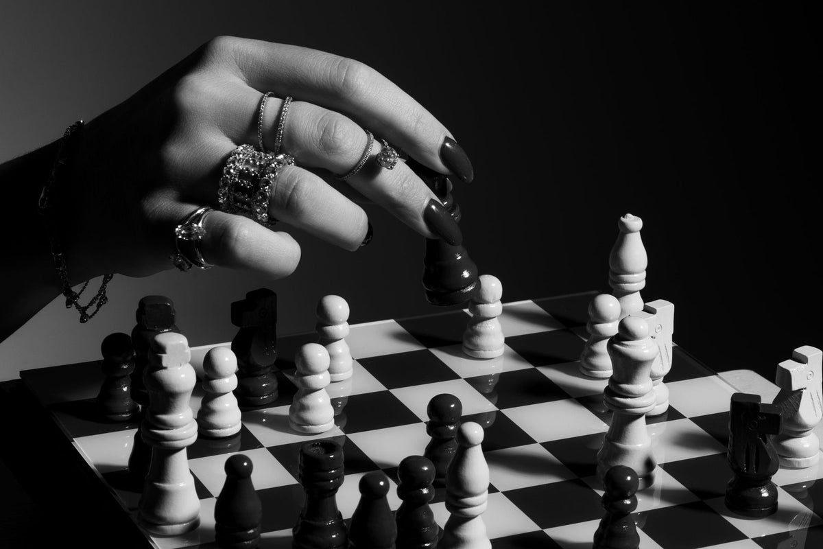 Main ornée de bagues diamants déplaçant un cavalier sur un échiquier, photo en noir et blanc