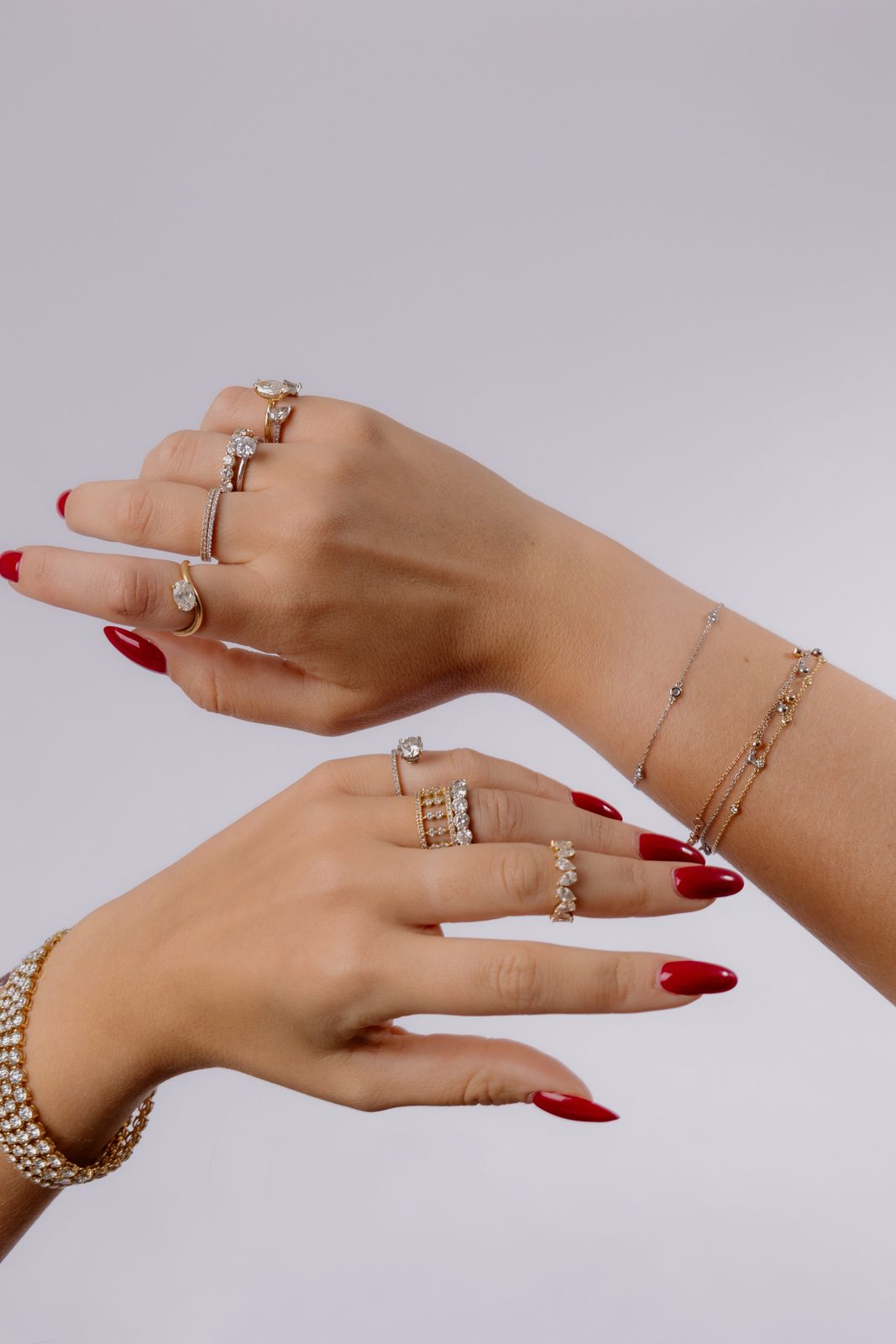 Deux mains croisées ornées de bagues fines, alliances diamants et bracelets, ongles rouges